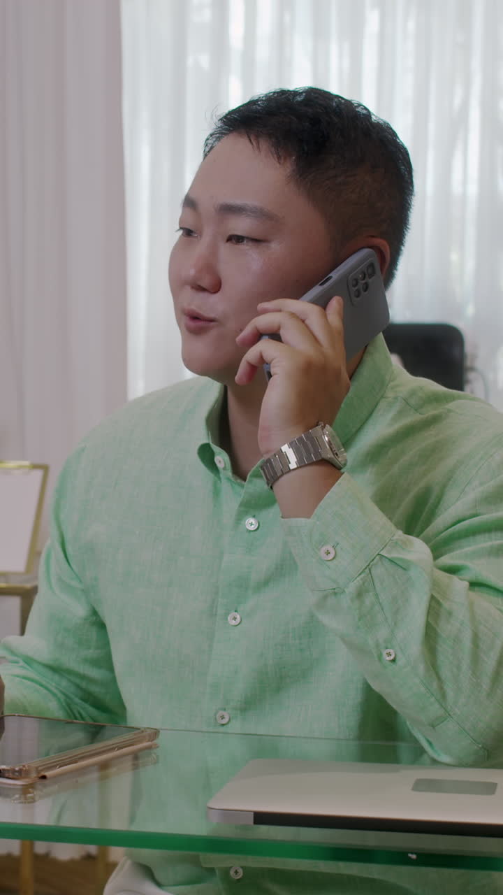 Businessman Talking on Smartphone and Checking Tablet at Desk