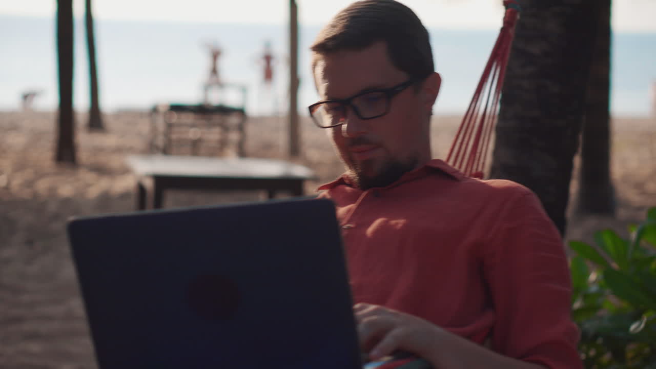 hombre trabajando en una computadora portátil en la playa en una hamaca
