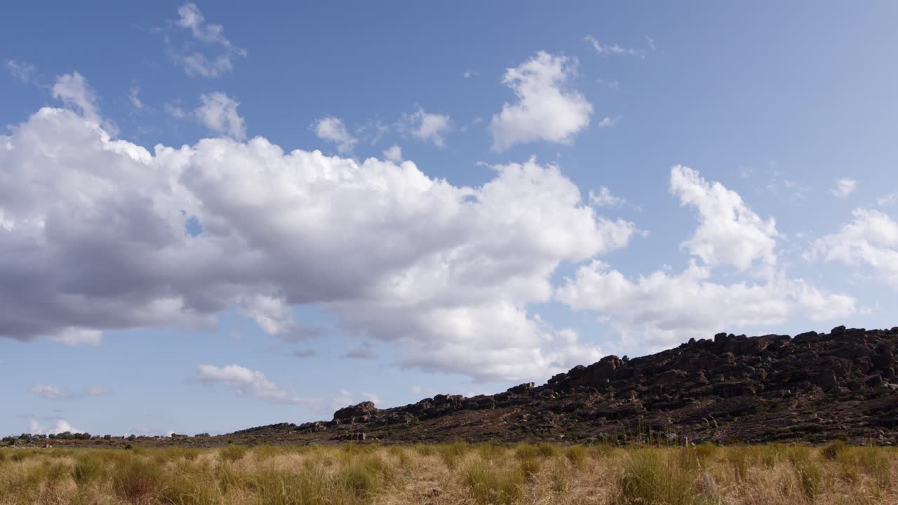 las nubes de lapso de tiempo se mueven sobre una plantación de té de arbusto rojo con una colina rocosa en el fondo
