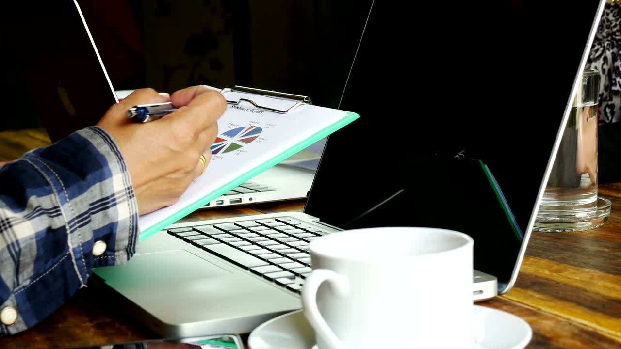 trabajador buscando informe de verano y escribiendo portátil con café de bebida.