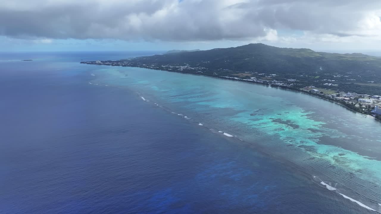 "A stunning aerial drone shot capturing the calm and crystal-clear emerald waters of Saipan’s west coast. Features beautiful coral reefs visible through the transparent sea."