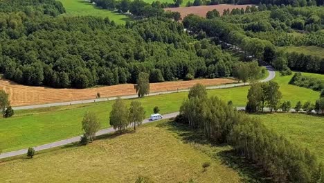 aerial shot of rv driving on a curvy country road surrounded by fields and trees