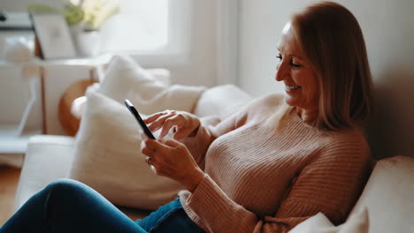 senior woman relaxing on couch and using smartphone