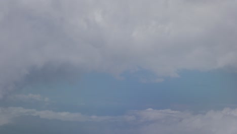 view of large clouds above and below outside of chromatic airplane window, santorini, greece, europe