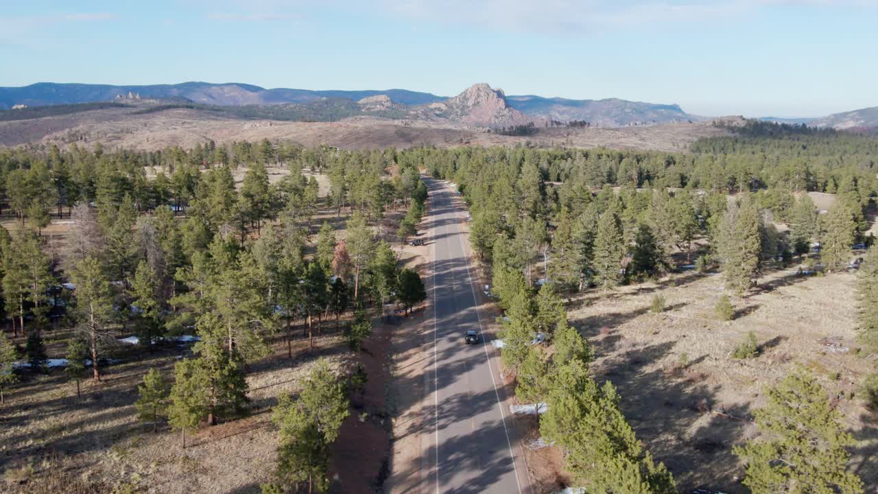 Aerial drone view of the Pike National Forest and a vehicle driving along a remote mountain highway. Forward dolly movement tracking a vehicle. Filmed in the Rocky Mountains of Colorado.
