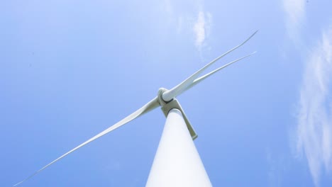 low angle looking up at wind turbine spinning blades renewable energy generator against blue sky