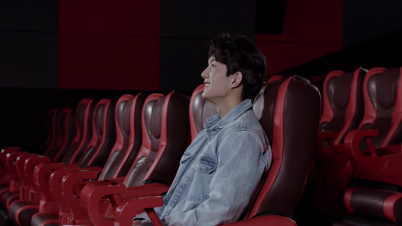 Giovane uomo allegro, eccitato e bello che sorride, godendosi un film al cinema. Siede da solo in una sala cinematografica vuota, emanando un senso di svago e intrattenimento.