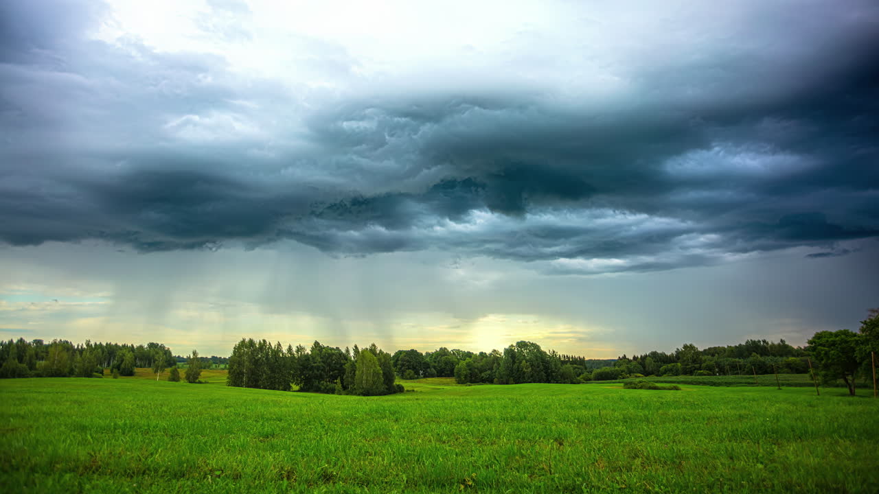 timelapse of green meadow landscape, stormy rain clouds floating over rural land, cinematic idyllic mood, nostalgic screensaver, yellow twilight on horizon