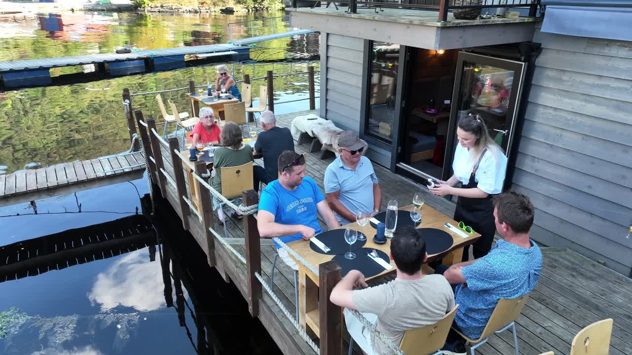 Drone gently approaches guests seated on a seafront terrace as a waitress pours white wine into their glasses
