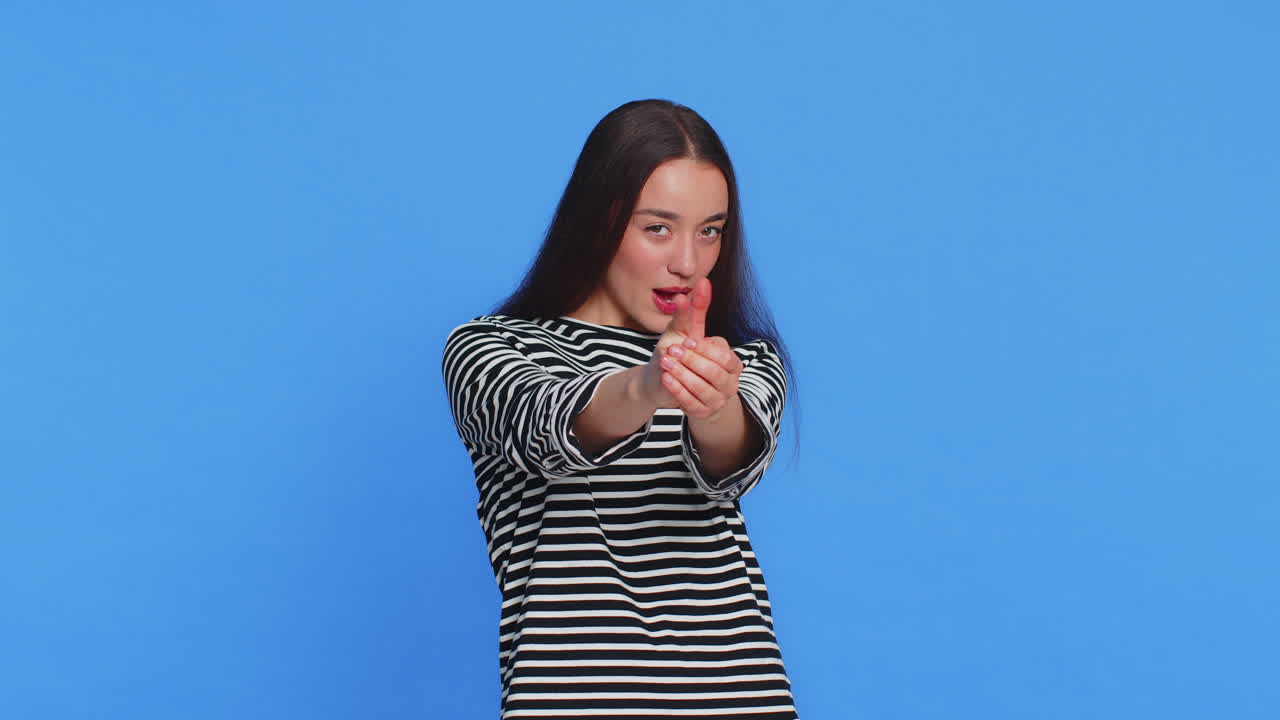 Young woman pointing around with finger gun gesture making choice shooting killing with hand pistol