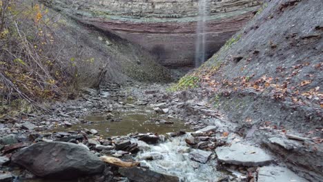 Rocky-mountain-valley-bedrock-with-small-skinny-waterfall,-low-to-ground-gimbal