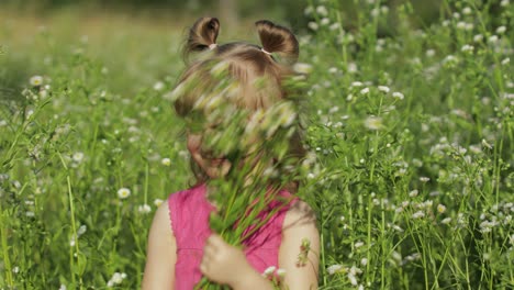 little blonde child girl in pink dress stay on flower chamomile grass meadow. bouquet of daisies