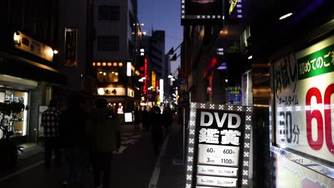 pedestrians walking past illuminated signs at dusk