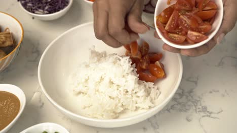 añadiendo tomates bebés a un tazón de arroz blanco creando una fusión asiática delicioso tazón poke