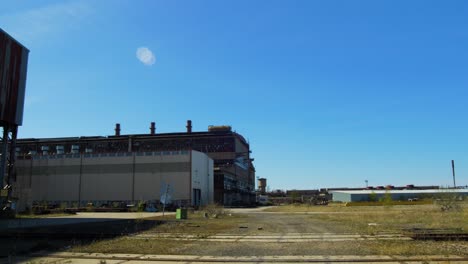 exterior view of abandoned soviet heavy metallurgy melting factory liepajas metalurgs territory, rust-covered warehouse buildings, sunny day, wide panoramic shot moving right