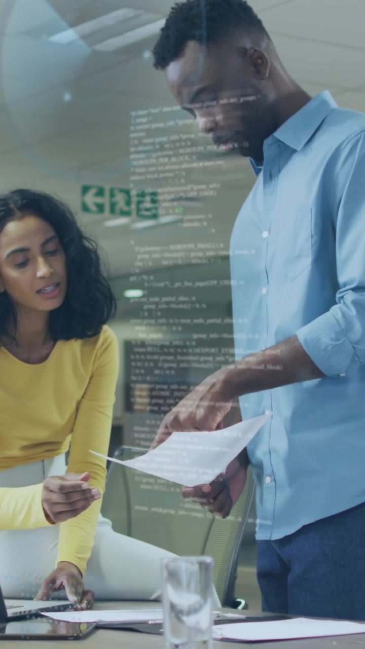 Vertical video: Woman passing paper to man, sparking office review with laptop and code on glass