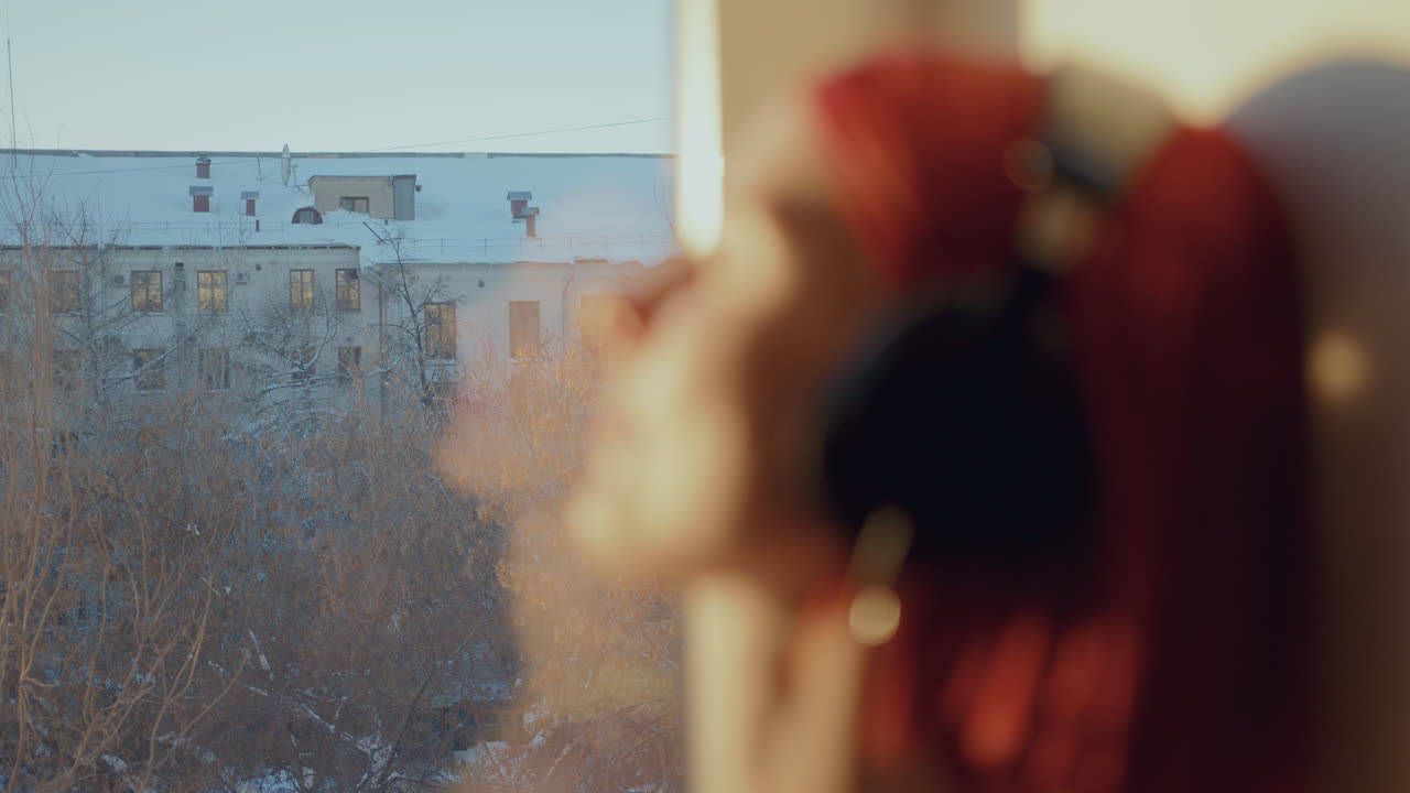 спокойная девушка в наушниках слушает музыку на солнечном подоконнике