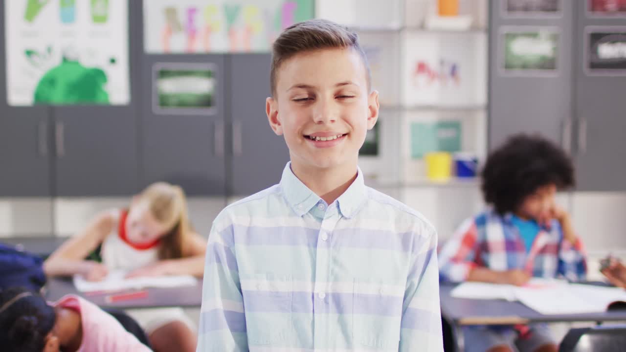 Portrait of happy caucasian schoolboy at desk in school classroom
