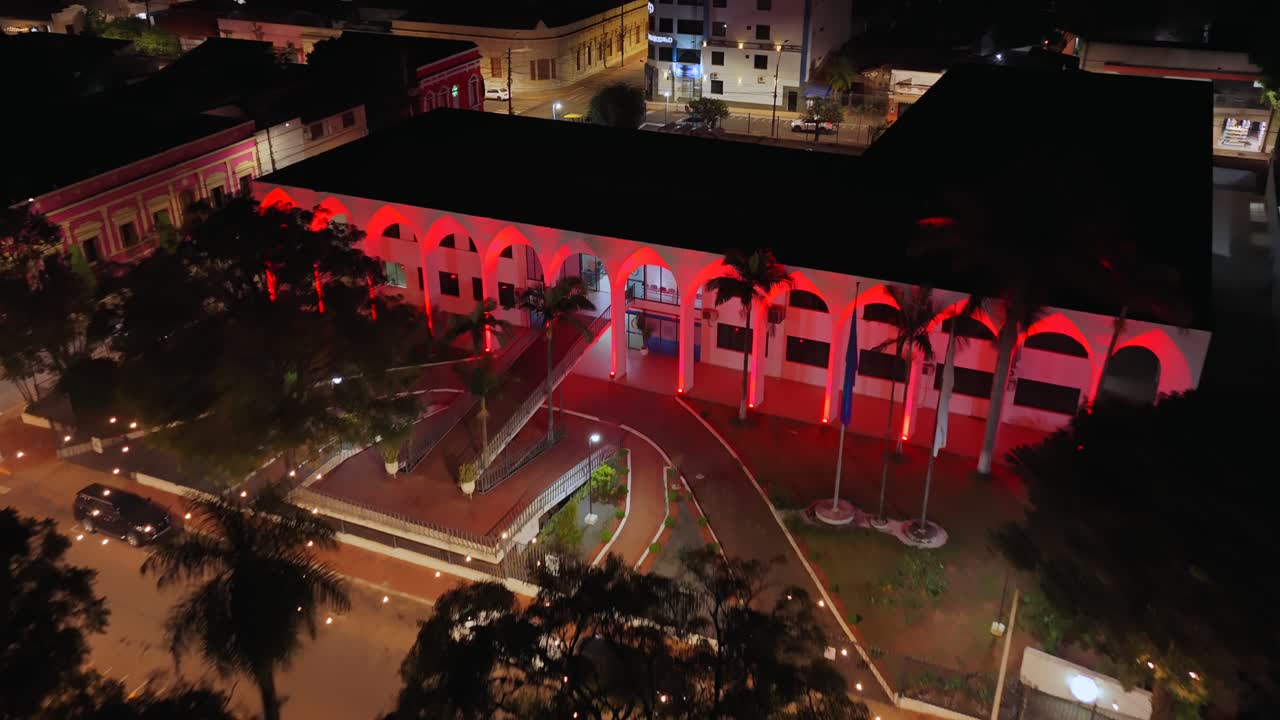 Backward aerial at night over Government of Guaira building and Plaza de la Libertad in Villarrica, Paraguay