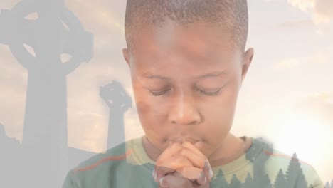 Animation-of-african-american-boy-praying-and-crucifixes-at-sunset