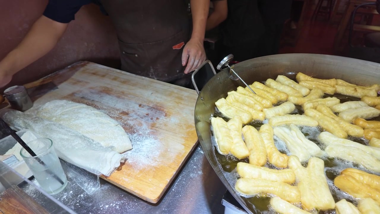 Close-up shot of street food vendor frying dough sticks in hot oil with flour dusting.
