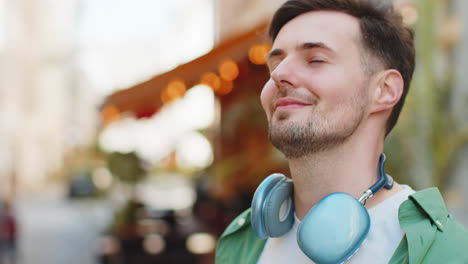 thoughtful happy smiling male tourist with wireless headphones around neck looking up on city street