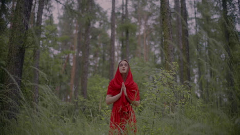 mujer con vestido rojo orando en el bosque