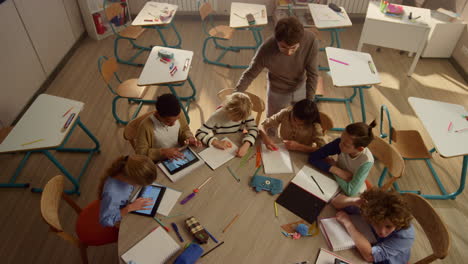 alumnos con blocs estudiando en una mesa redonda. niños usando tabletas digitales