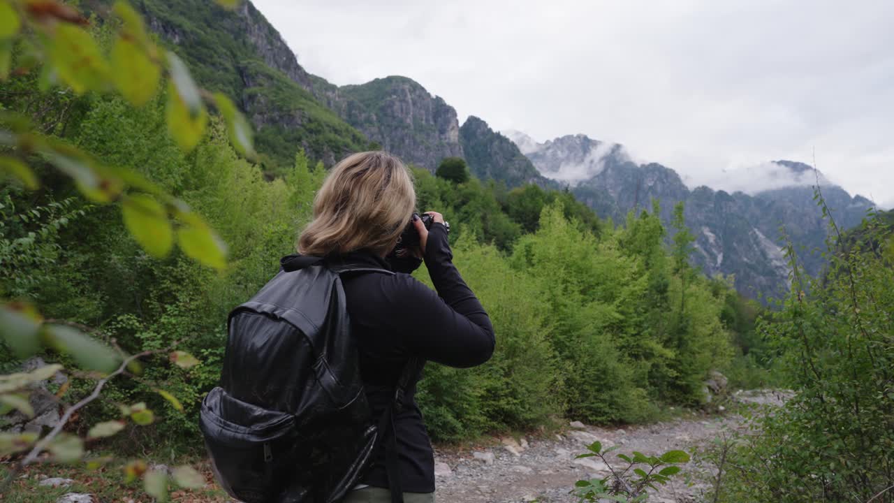 Female photographer with a backpack takes pictures of mountains in Montenegro