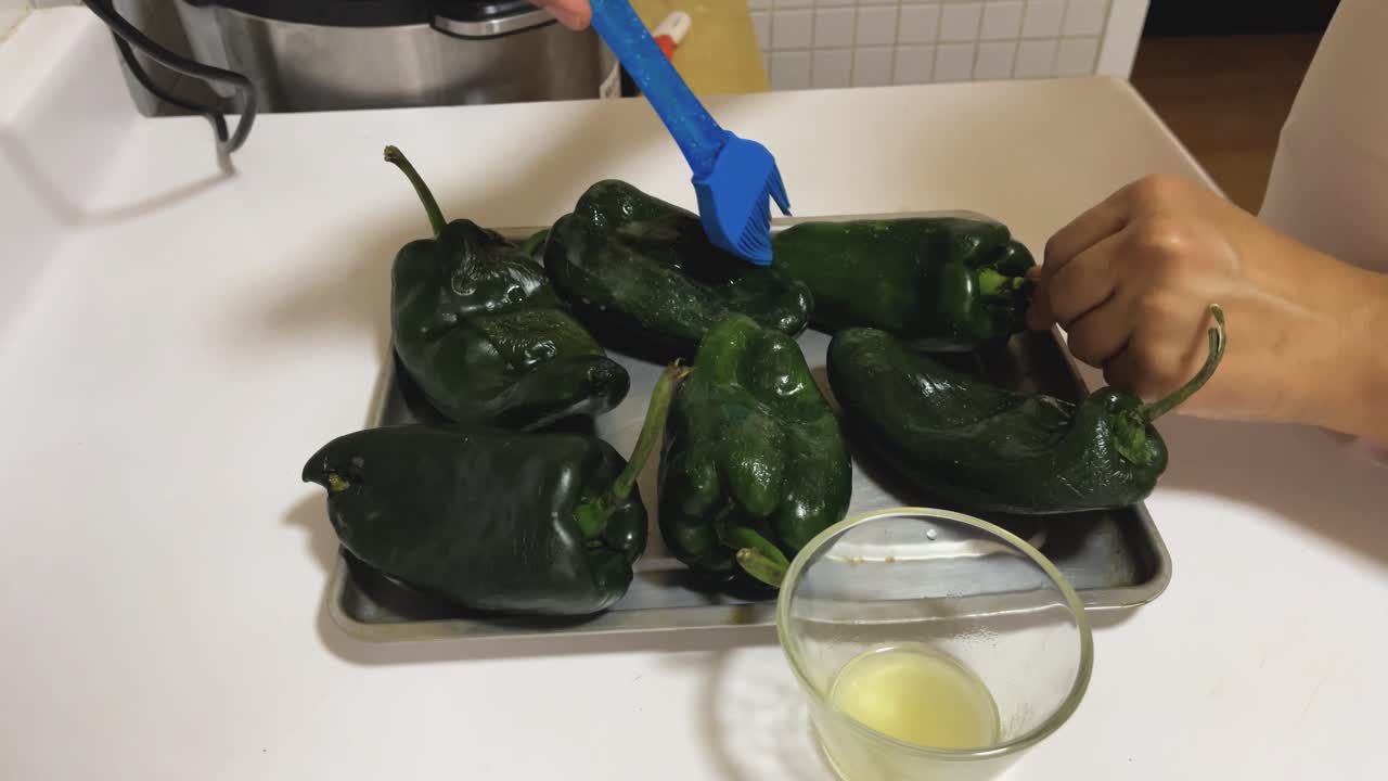 Poblano peppers arranged on a baking sheet. Each pepper is brushed with a silicone spatula