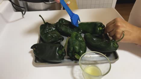 poblano peppers arranged on a baking sheet. each pepper is brushed with a silicone spatula