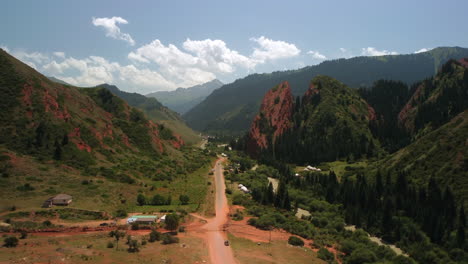 Drone-footage-of-red-mountains,-green-trees,-and-green-hills-in-a-sunny-day-with-little-clouds