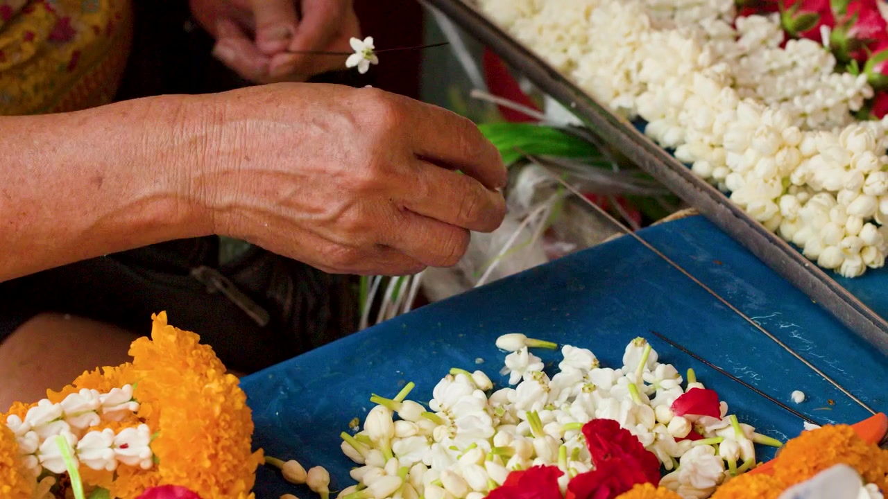 Primo piano di mani che assemblano offerte floreali con gelsomino e calendula a Pak Khlong Talat