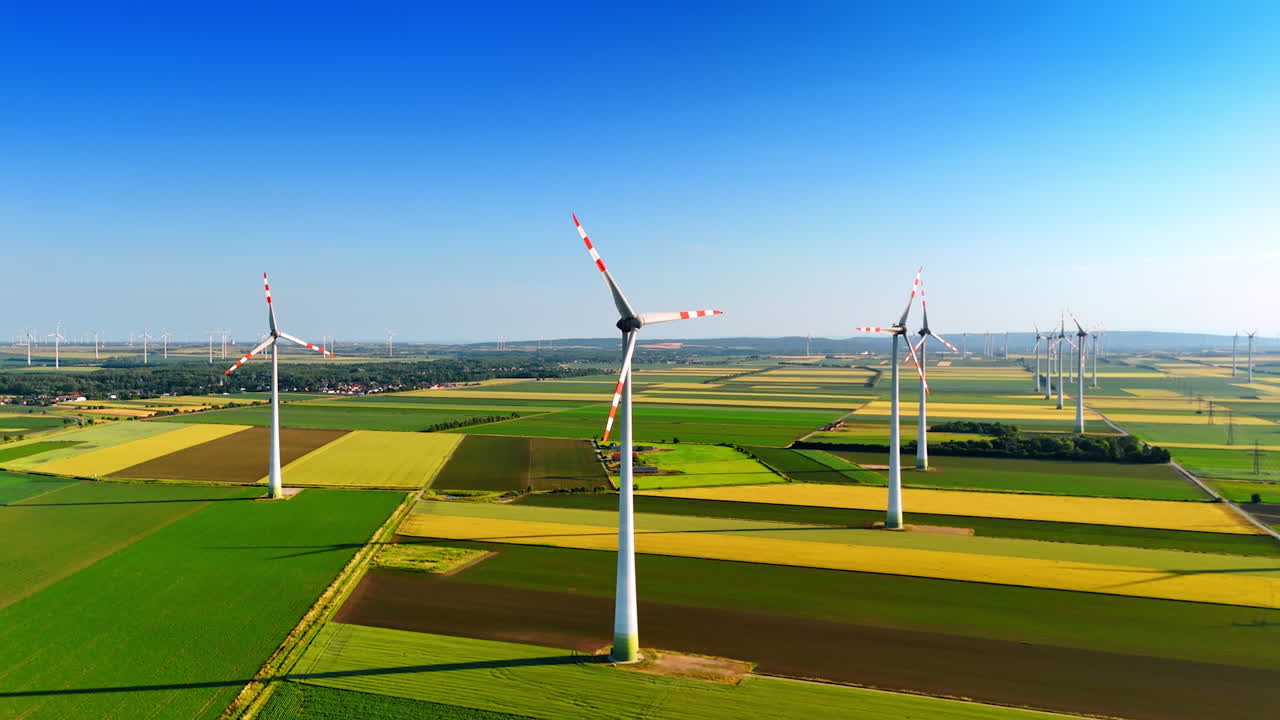 Turbines produce energy in fields. Turbines spin under a clear blue sky, transforming wind into renewable energy across green fields