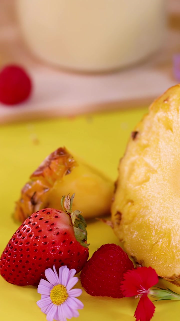 Rodajas de piña fresca y bayas mixtas caen sobre una superficie amarilla brillante en un primer plano colorido