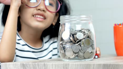 asian little girl putting the coin in to a glass jar shallow depth of field select focus on jar