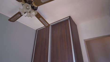 slow motion camera reveals vintage-style ceiling fan and floor-to-ceiling wardrobe with dark wood panels in a minimalist bedroom interior, soft lighting, clean lines
