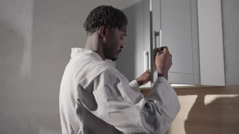 close-up of man in bathrobe with short hair, facing sideways. strong lighting emphasizes his profile, with shadows on the wall. minimalist background adds depth and focus on his features