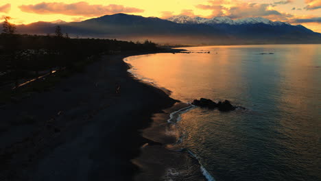 Drone-shot-of-sea-with-snow-capped-mountain-background-and-orange-sky