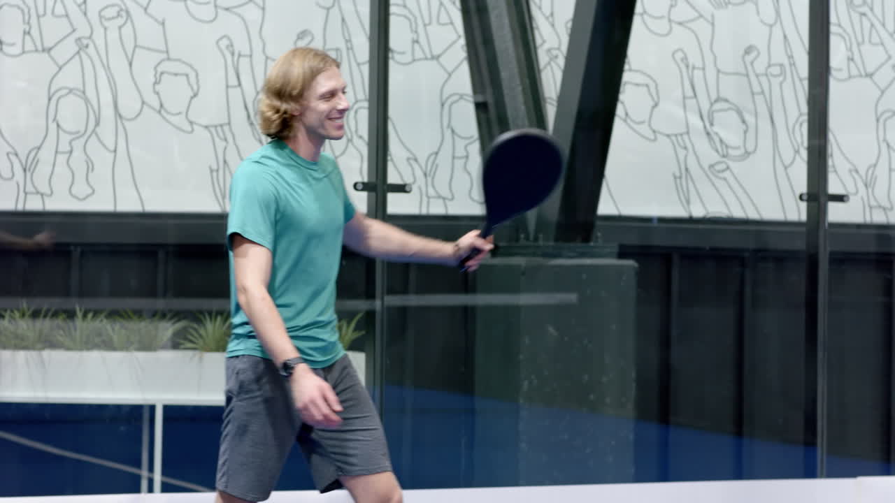 Young man playing padel tennis, swinging racket with focus and determination, at indoor court