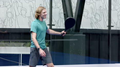 young man playing padel tennis, swinging racket with focus and determination, at indoor court