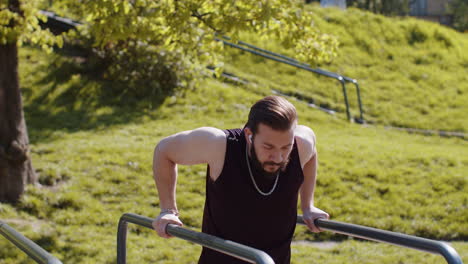 Athletic-lebanese-man-in-sportswear-practicing-dips-on-parallel-bars,-training-triceps-on-playground