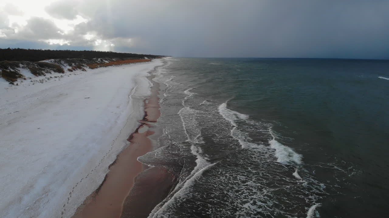 Winter beach scene with stormy sea and snow-covered sand