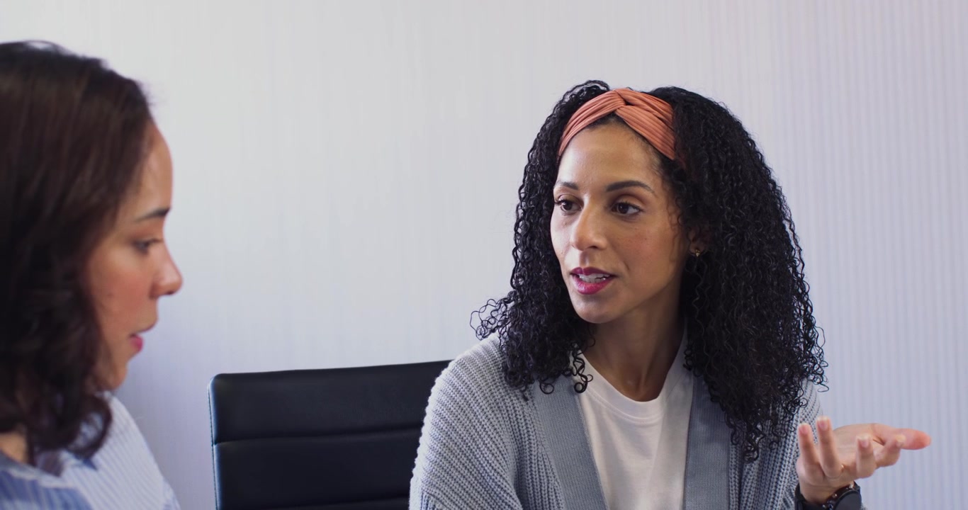 Personale femminile afroamericano in una stanza, a sinistra una persona parla e guida, a destra una persona chiarisce con una fascia per capelli
