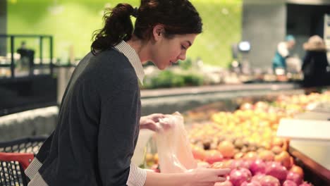 Young-beautiful-brunette-girl-in-her-20's-picking-out-tangerines-into-a-plastic-bag-at-the-fruit-and-vegetable-aisle-in-a