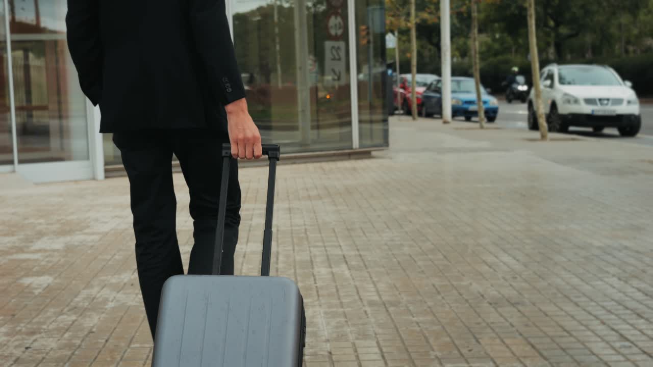 Hombre turista con maleta en España, un viajero con equipaje y chaqueta de traje en una calle de negocios yendo a un hotel, oficina o terminal de aeropuerto, disfrutando del ambiente vibrante
