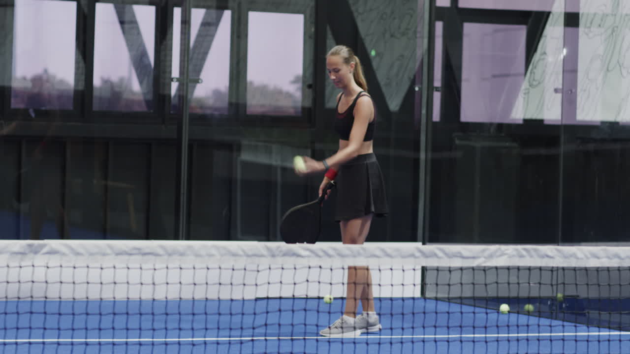 Young woman playing padel tennis, swinging racket on indoor court