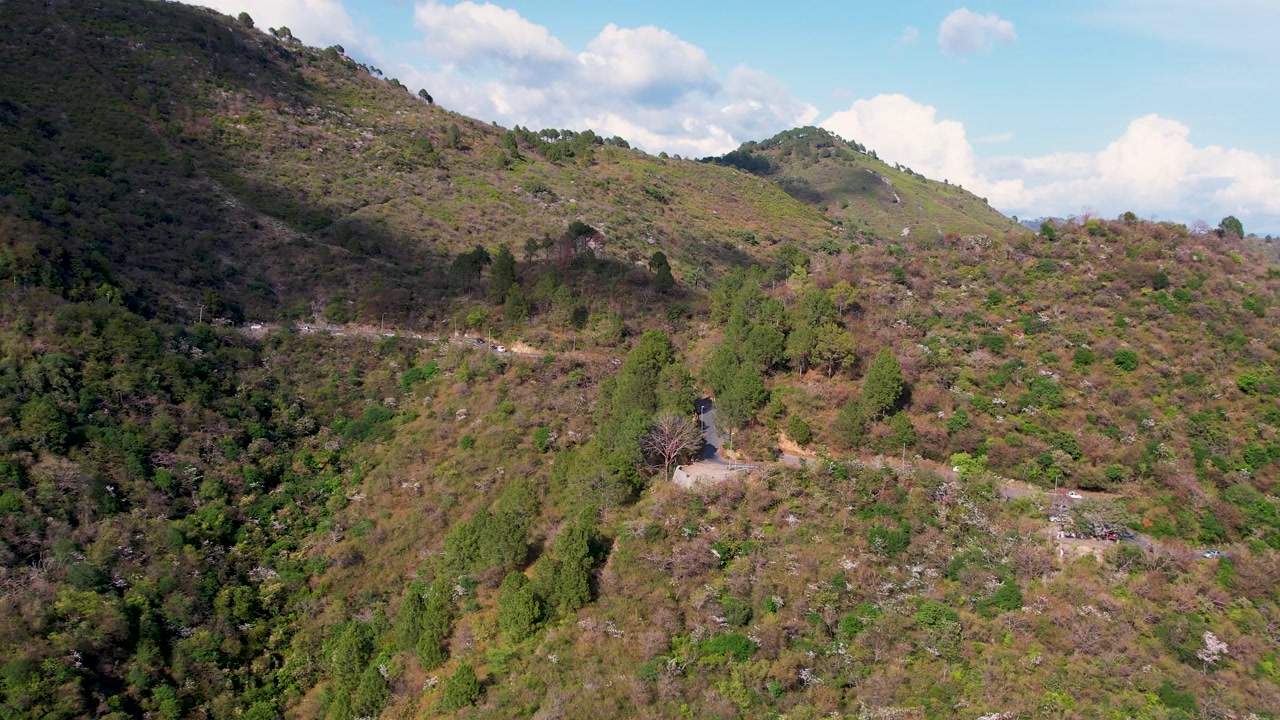 Winding road cuts across green and brown hillside with scattered trees in Margalla Hills, Islamabad, Pakistan