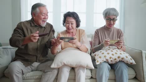 happiness asian retired friend enjoy playing and competition game smartphone mobile online together on sofa in living room home interior background,asian group playing game together home isolate idea