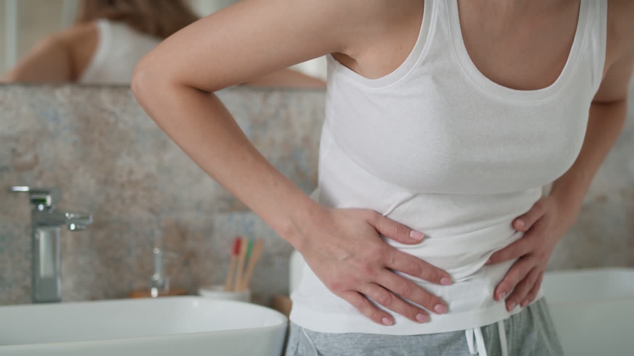 Young caucasian woman standing in the bathroom and feeling pain in the stomach.